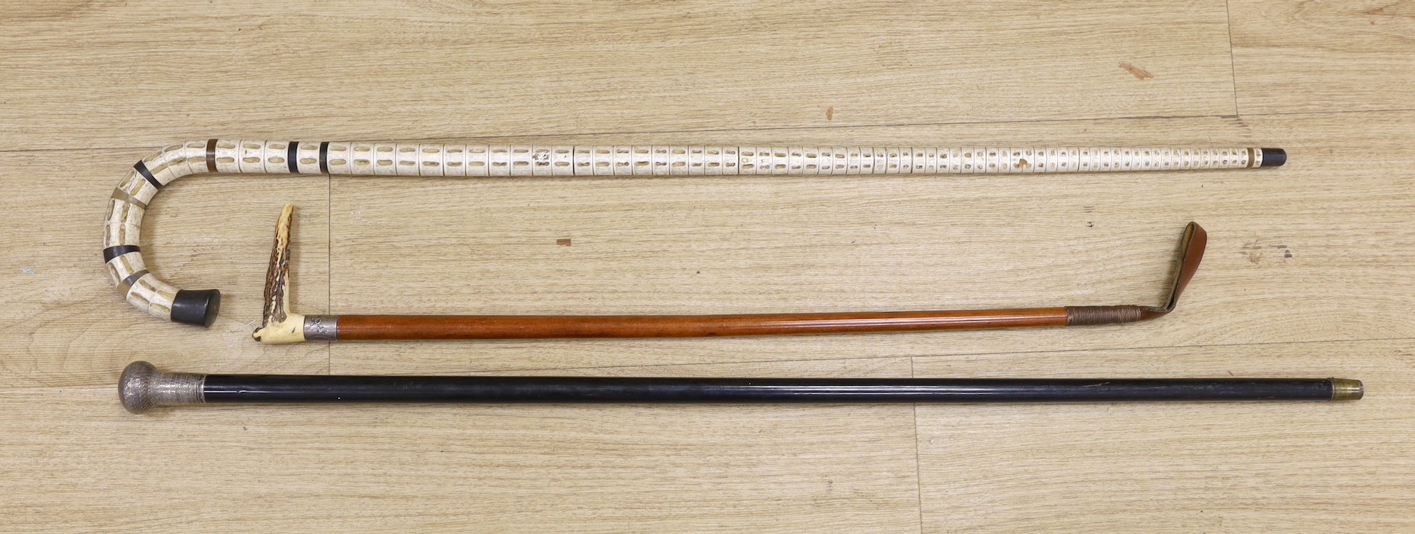 A silver mounted ebony walking cane, a shark vertebrae walking stick and a stag antler mounted malacca riding crop